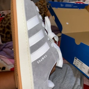 Gråa Adidas Campus sneakers - Ett par gråa Adidas Campus sneakers med vita detaljer och snörning. Skorna har en gummisula och är i nyskick.