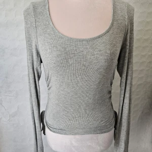 Grå ribbad tröja från Shein - En grå ribbad tröja från Shein med långa ärmar och rund halsringning. Tröjan har en åtsittande passform och justerbara knytband på sidorna.