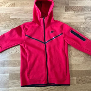 Röd Nike tech fleece - Säljer nu min Nike tech har haft på mig den bara 2-3 gånger annars aldrig använt. Storlek S men passar också M. Helt original köpt från JDsports för 1500kr. Pris kan diskuteras