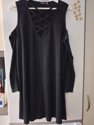 Svart klänning med snörning Boohoo - Svart kort klänning från Boohoo med v-ringning och dekorativ snörning framtill. Klänningen har lång ärm med cold shoulder-detalj och är tillverkad i ett mjukt, ribbat material. Perfekt för dig som gillar en edgy och trendig stil.