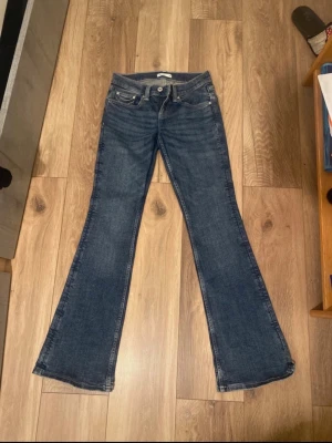 Mörkblå bootcut jeans - Säljer ett par mörkblå bootcut jeans med låg midja. Jeansen har en snygg tvätt, klassisk femficksdesign och har ett fint broderat mönster/design på bakfickorna. De är tillverkade i denim med lätt stretch för en skön passform. Perfect skick! 