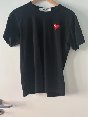 Cdg T-shirt  - Köpt för 1000kr på NK. Svart t-shirt med rund hals och korta ärmar. På bröstet sitter ett litet rött hjärta med ögon, vilket ger en unik och lekfull touch. T-shirten har en enkel och clean design som passar till det mesta.