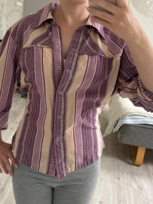 Randig skjorta med knyte  - Söt lila randig skjorta med knyte bak som man kan anpassa efter sin storlek, omsydd. S-M. Trekvartärm. Går att diskutera pris. Insta, TikTok & Vinted: Melioraofficials 