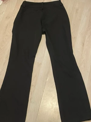 Svarta kostymbyxor bootcut från bik bok - Snygga svarta kostymbyxor med bootcut passform och hällor för skärp. Klassisk design utan synliga detaljer framtill. Perfekta till en dressad look och passar till många olika stilar.