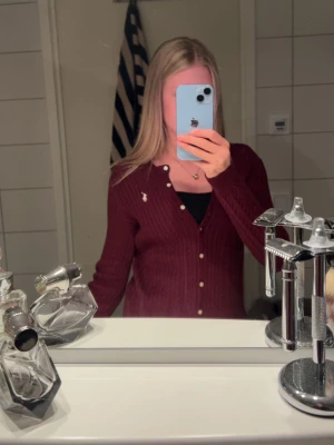 Vinröd kabelstickad kofta Polo Ralph Lauren - Vinröd kabelstickad kofta från Polo Ralph Lauren med klassisk vit logga broderad på bröstet. Koftan har rund halsringning, pärlemorknappar och ribbade muddar. Koftan är aldrig använd har bara provat den. Sitter som en tröja i storlek xs.