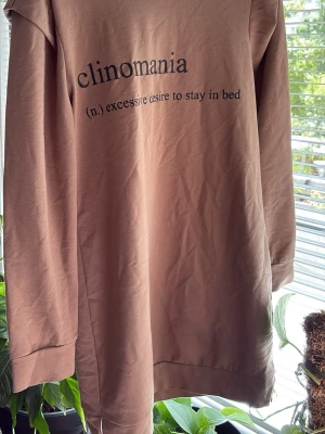  nattlinne med tryck - Mysigt nattlinne i en brun nyans med svart texttryck på framsidan: 'clinomania (n.) excessive desire to stay in bed'. Långärmad modell med rund halsringning, perfekt för lata dagar hemma.