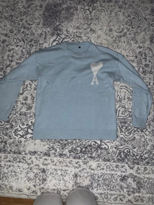 Baby blå stickad tröja - Säljer en babyblå stickad tröja som har ett vitt hjärta med ett stort A under. Man kan använda den på både sommaren och vintern. Den är väldigt skön att ha på sig.