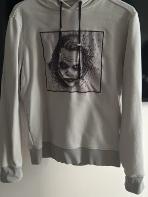 Ljusgrå hoodie med tryck - Säljer en limitato hoodie med en mycket speciellt tryck. Den är riktigt fet till nästan vad som. är lite urtvättad med är inget som syns kan kännas bara lite nopprig där inne i hoddien. Har en liten liten defekt vid lappen som knappt syns. 