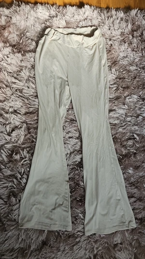 Beiga utsvängda leggings - Säljer ett par beiga leggings med utsvängda ben och två bakfickor med knappdetaljer. Mjukt och stretchigt material som sitter skönt på kroppen. 