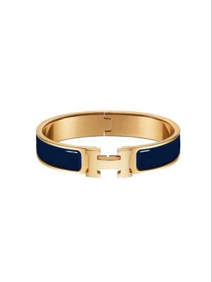 Guldigt H-armband mörkblå guld  - Snyggt armband i guldton med mörkblå emaljdetaljer och ett stilrent H-format spänne framtill. Armbandet har en elegant och modern design som passar perfekt till olika outfits. Materialet är metall med emaljinslag och färgerna är guld och marinblå.