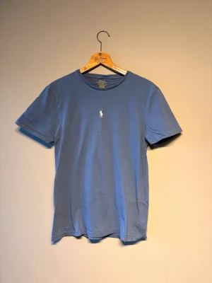 Blå t-shirt från Polo Ralph Lauren - Snygg blå t-shirt från Polo Ralph Lauren med klassisk rund hals och den ikoniska broderade loggan i vitt på bröstet. Modellen är custom slim fit och tillverkad i mjuk bomull som känns skön mot huden. Perfekt till jeans eller shorts.