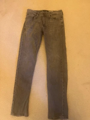 Grå raka jeans med fem fickor - Snygga grå jeans i rak modell med klassisk femficksdesign och normal midja. Jeansen har diskreta sömmar och är tillverkade i ett mjukt denimtyg som ger en avslappnad look. Perfekta att matcha med en hoodie eller t-shirt.