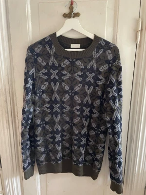 Mönstrad stickad tröja Dries Van Noten - Säljer en unik stickad tröja från Dries Van Noten i storlek Small. Tröjan har ett coolt blommigt mönster i svart, grått och olivgrönt. Rund halsringning och ribbade muddar vid ärmslut och nederkant. Perfekt för dig som gillar statement-plagg!