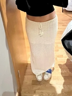 Vit stickad långkjol med snörning - Säljer en vit stickad långkjol med snygg snörning i midjan. Kjolen har en rak passform och är gjord i ett mjukt material som ger en avslappnad men ändå stilren look. Perfekt att matcha med en croppad topp eller hoodie. Perfekt till stranden eller bara som en vanlig outfit! Använd 1 gång!