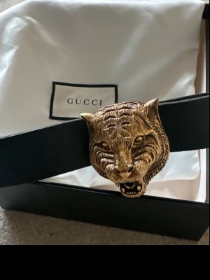 GUCCI Feline Head buckle skärp | 85cm - Gucci Feline Head Buckle Belt – svart läder med guldfärgat spänne. Bältet är i mycket fint skick och har endast använts vid enstaka tillfällen – aldrig som vardagsbälte. • Storlek: 85 • Originalpris: ca 5 000 kr • Inköpt på Guccis hemsida omkring 2016–2017. Ett av Guccis mer ovanliga Feline Head-bälten som inte längre finns i ordinarie sortiment. Säljs i mycket fint skick. Kommer med dust bag och låda.