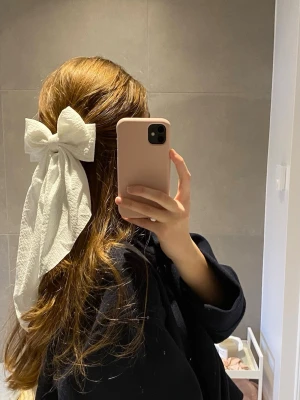 Stor vit hårrosett med långa band - Säljer en stor vit hårrosett med långa band som ger en riktigt söt och trendig look. Rosetten är gjord i ett tyg med lite struktur och fästs enkelt i håret. Perfekt för att piffa till frisyren och ge en extra touch till din outfit.