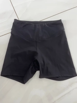 Svarta cykelshorts i syntetmaterial - Svarta, tighta cykelshorts med hög midja. Tillverkade i ett stretchigt syntetmaterial som passar perfekt för träning eller en sportig look. Enkla och stilrena utan synliga loggor eller detaljer.
