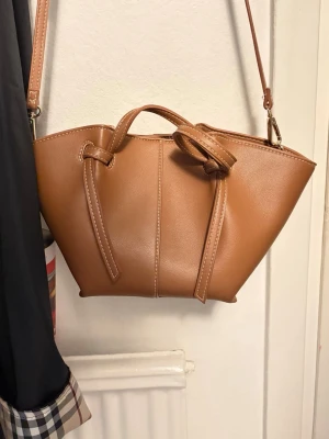 Brun handväska med axelrem - Snygg brun handväska i slätt konstläder med justerbar axelrem och även kortare handtag. Köpt på Åhlens för 499kr och knappt använd✨