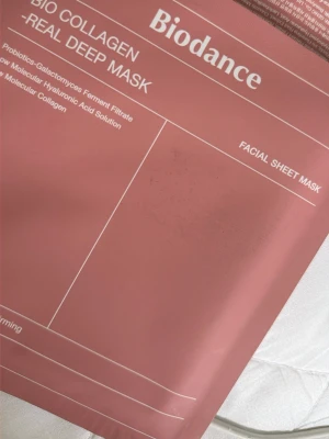 Biodance Bio Collagen Sheet Mask - Biodance Bio Collagen Real Deep Mask är en ansiktsmask i arkmaterial som innehåller probiotika, galactomyces fermentfiltrat, hyaluronsyra och kollagen. Förpackningen är rosa och masken är designad för att ge näring och återfukta huden.