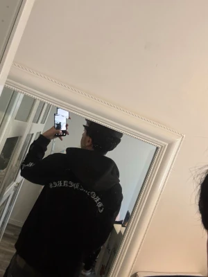 Svart Chrome 1982 hoodie med vit text - Säljer en svart Chrome 1982 hoodie med dragkedja och vit text i gotisk stil på både ryggen och ena ärmen. Hoodien har en huva och en avslappnad passform, perfekt för en streetwear-look. Passar dig som gillar edgy och unik stil. Kan diskutera pris
