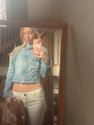 Ljusblå croppad jeansjacka - Trendig ljusblå jeansjacka med croppad passform och hög krage. Jackan har dragkedja framtill och markerade sömmar som ger en snygg siluett. Perfekt för dig som vill ha en stilren och modern look.