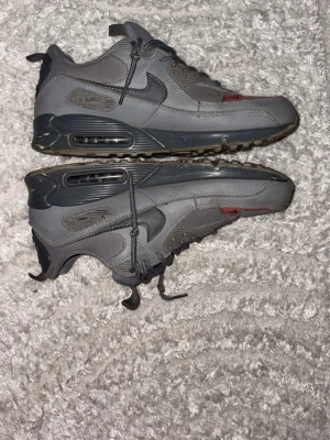 Grå Nike Air Max sneakers - Snygga grå Nike Air Max sneakers med klassisk design och synlig luftdämpning i sulan. Skorna har snörning, detaljer i mörkgrått och en diskret rosa accent framtill. Tillverkade i en mix av syntet och textil för en sportig look.