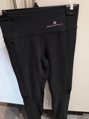 Svarta leggings från Ronhill - Säljer ett par svarta leggings från Ronhill med hög midja och diskret logga framtill. De är tillverkade i ett stretchigt och mjukt material som passar perfekt för träning eller chill. Snygg passform och klassisk look.