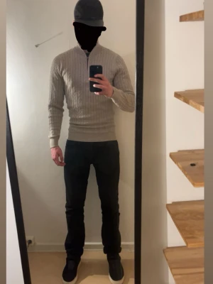 Beige stickad tröja med dragkedja - Snygg beige stickad tröja med halv dragkedja i halsen och ribbade muddar. Tröjan har ett diskret kabelstickat mönster och sitter slimmat på kroppen. Perfekt för lager-på-lager och passar till både jeans och chinos.