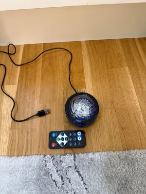 Projektorlampa med fjärrkontroll - Cool projektorlampa med USB-sladd och fjärrkontroll. Lampan har en rund, svart och transparent design och kan projicera röda ljuseffekter på väggar eller tak. Perfekt för att skapa en häftig stämning i rummet. Materialet är plast.