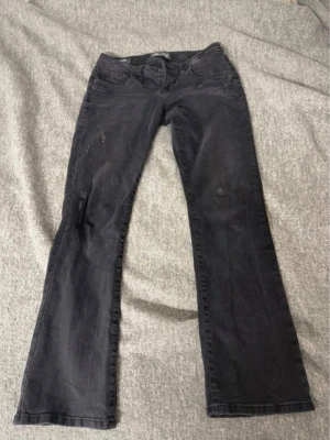 Svarta bootcut jeans med slitningar - Säljer ett par svarta bootcut jeans med lätt slitna detaljer på benen. Jeansen har klassisk femficksdesign och låg midja. Snygg passform som sitter tajt upptill och släpper vid vaden. Perfekta till en avslappnad och trendig look. Dem är i storlek 27x30, dem är slutsålda och nypris är 799kr. 🥰pris kan diskuteras vid snabb affär!