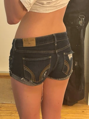Mörkblåa jeansshorts från Hollister - Säljer ett par mörkblåa jeansshorts från Hollister med slitna detaljer och råa kanter. 