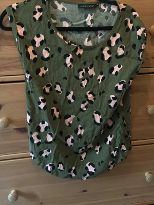 Grön leopardmönstrad topp från Jazlyn - Cool grön topp från Jazlyn med leopardmönster i svart och ljusrosa. Modellen är ärmlös med rund halsringning och har en avslappnad passform. Perfekt för dig som vill sticka ut med ett trendigt mönster.