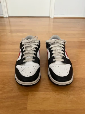 Nike dunk low - Storlek 45 - Säljer ett par Nike Dunk Low i svart/vit/röd färgkombination i storlek 45. Skorna är i bra skick med normalt slitage från användning. Sulorna är fortfarande i bra skick och skorna är bekväma och redo för många fler användningar. Viss crease/slitage på ovandelen och mindre märken finns, vilket syns på bilderna. Inga större skador, hål och defekter förekommer.