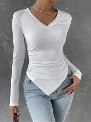 Vit långärmad topp - Trendig vit långärmad topp med v-ringning och ribbad struktur. Toppen har en asymmetrisk nederkant och smickrande drapering i midjan. Perfekt att styla med jeans eller kjol för en clean look.