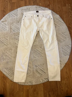 Vita jeans från Lee - Säljer ett par snygga vita jeans från Lee med klassisk femficksdesign och raka ben. Jeansen har Lee-logga på bakfickan och är tillverkade i bomull. Perfekta för dig som vill sticka ut med en fräsch look.