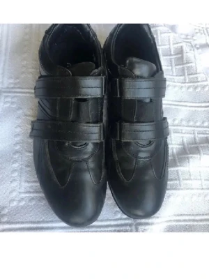 Svarta läder sneakers med kardborreband 41 - Säljer ett par svarta sneakers med två breda kardborreband över foten. Skorna har en sportig design med rundad tå och mönstrad sula för bra grepp. Tillverkade i syntetmaterial med diskreta sömmar som detalj. Perfekta för dig som gillar enkel och stilren look.