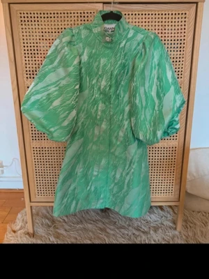 Grön klänning från Ganni - Superfin grön kortklänning från Ganni med unikt mönster och puffiga korta ärmar. Klänningen har en liten krage och en passform som ger en väldigt fin siluett. Perfekt för dig som vill sticka ut på sommarens fester! Storlek XS men passar en S