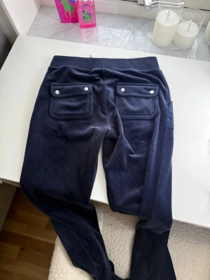 Mörkblå Juicy Couturemed fickor - Mörkblå mjukisbyxor i mjuk velour med stora fickor både fram och bak. De är bara andvända fåtal gånger.