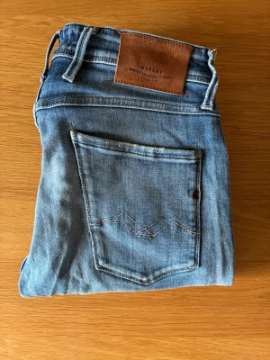 Replay anbass med slitingar  - Snygga blå jeans från Replay med klassisk femficksdesign och läderpatch bak i midjan. Jeansen har raka ben och är tillverkade i mjukt denimtyg. Perfekta för en avslappnad och trendig look.