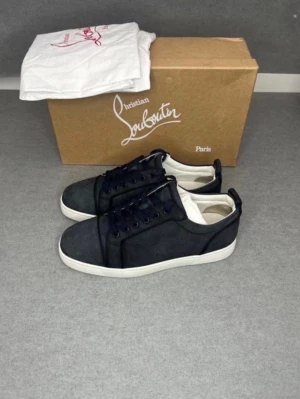 Svarta Christian Louboutin sneakers - Snygga svarta sneakers från Christian Louboutin med vita sulor och svarta skosnören. Skorna har en stilren design med ovandel i läder och textil, samt diskreta detaljer. Perfekta för dig som vill ha en exklusiv och trendig look. Allt og. Storlek 41 passar 42