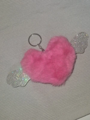 Nyckelring - Supergullig nyckelring med ett fluffigt rosa hjärta i mjukt material och glittriga silvriga vingar på sidorna. Perfekt att hänga på väskan eller nyckelknippan för en extra söt touch. Metallring för enkel fastsättning.