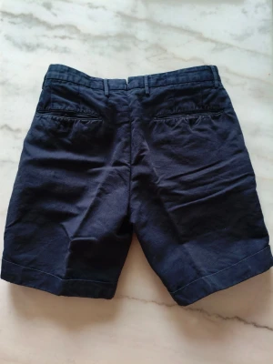 Mörkblå bomullsshorts med dragkedja - Mörkblå shorts i bomull med klassisk passform och dragkedja framtill. Snygga sömdetaljer vid midjan och enkel design som funkar till många olika stilar.Nypriset var 3300 kr 