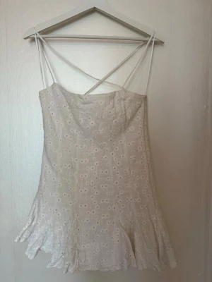 Vit broderad sommarklänning - Söt vit klänning med tunna axelband som korsas i ryggen. Klänningen har broderade blommor och lätt utsvängd kjol. Perfekt för varma dagar och har en romantisk, luftig känsla.