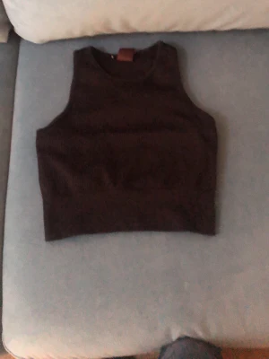Svart ribbad linnetopp - Snygg svart ribbad linnetopp med ärmlös design och rund halsringning. Perfekt att styla till jeans eller kjol för en trendig look. Materialet är mjukt och stretchigt för skön passform.
