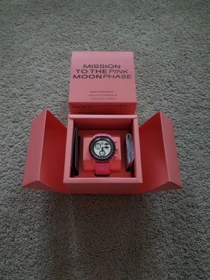 Omega x Swatch Pink Moonphase klocka - Säljer en Omega x Swatch MoonSwatch Mission to the Pink Moonphase. Klockan har rosa boett och armband, vit urtavla med svarta detaljer och kronograffunktion. Kommer i originalförpackning med manual och certifikat.
