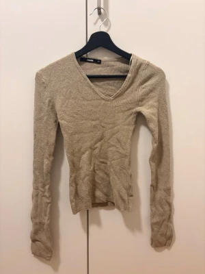 Beige stickad tröja V-ringning Bik Bok - Säljer en beige stickad tröja från Bik Bok med smal passform och V-ringad hals. Tröjan har långa ärmar och är tillverkad i ett mjukt, tunt stickat material som passar perfekt till lager på lager. Enkel och stilren design.