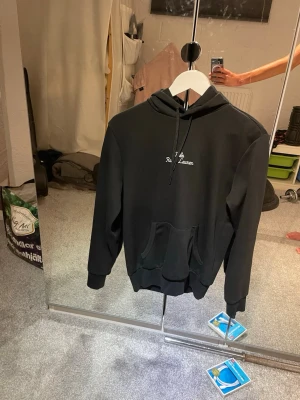 Svart hoodie från Ralph Lauren - Snygg svart hoodie från Ralph Lauren med broderad vit text på bröstet. Klassisk känguruficka framtill, ribbade muddar och justerbar huva med snören. Perfekt för en avslappnad och stilren look. Stor i storlek är som xs.
