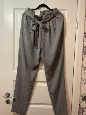 Grå byxor med knytband Bik Bok - • Helt nya •Snygga grå byxor från Bik Bok med hög midja och brett knytband i midjan. Byxorna har raka ben och resår i midjan för extra komfort. Perfekta för en avslappnad och trendig look.