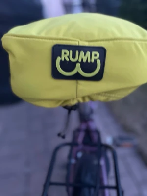 Gul sadelöverdrag från RUMP - Säljer ett grönt sadelöverdrag från RUMP med svart och gul logga. Överdraget är gjort i ett vattenavvisande material och har dragsko för att sitta stadigt på cykelsadeln. Perfekt för att hålla sadeln torr och fräsch under regniga dagar. Ni får gjärna sänka priset 