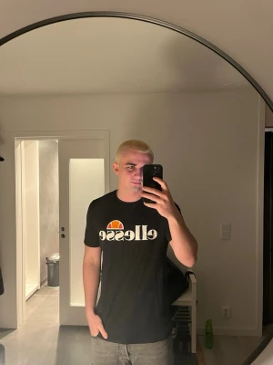 Svart Ellesse t-shirt med logga - Svart t-shirt från Ellesse med stor vit logga och orange detalj på bröstet. Klassisk rund hals och korta ärmar. Perfekt för en avslappnad och sportig stil.